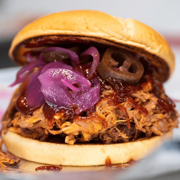 Close-up of a Warehouse BBQ pulled pork sandwich with pickled red onions and jalapeños.