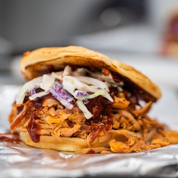 Close-up of a Warehouse BBQ pulled pork sandwich with coleslaw and barbecue sauce on foil.