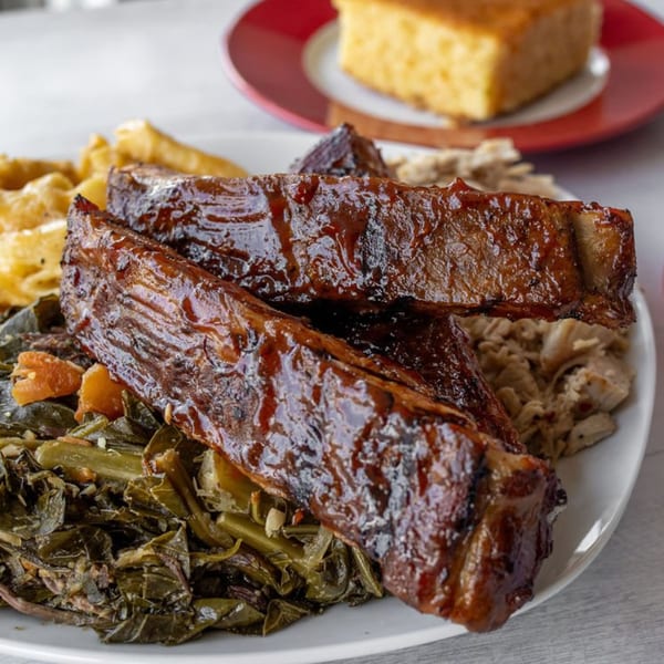 Warehouse BBQ ribs with collard greens, mac and cheese, and cornbread in the background.