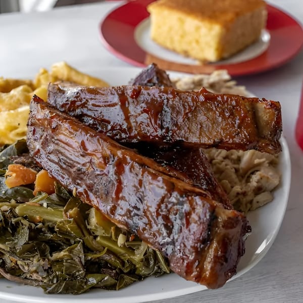 BBQ ribs with collard greens, macaroni and cheese, and cornbread on a white plate.