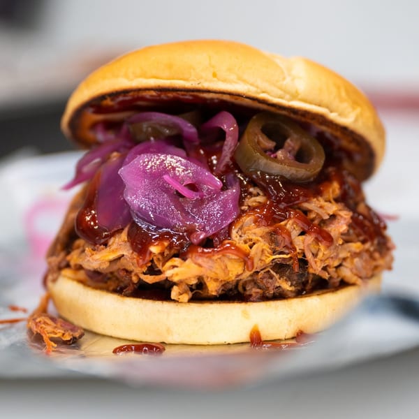 Close-up of a Warehouse BBQ pulled pork sandwich with pickled red onions and jalapeños.