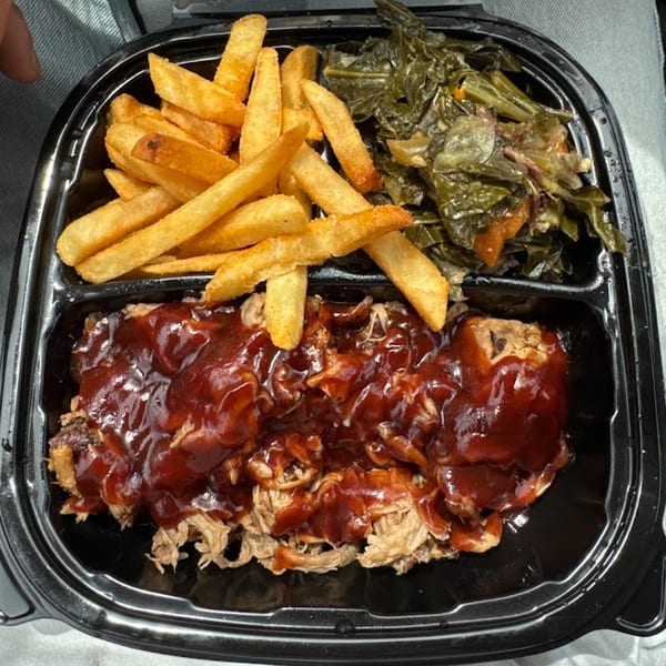 Warehouse BBQ pulled pork with barbecue sauce, french fries, and collard greens in a to-go container.